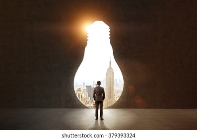 A man with hands in pockets standing in front of a huge keyhole, New York and sky seen through it. Black background. Back view.  Concept of finding the way