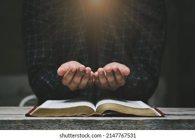 Man hands praying to god with the bible. Yellow lights and sparkles coming on Believe in goodness. Holding hands in prayer on a wooden table. Power of hope or love and devotion.  - Shutterstock ID 2147767531
