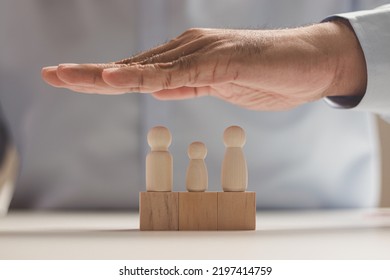 The Man Hands Protect Over Wooden Figures. Planning, Saving Family, Quality Family, Hedging, Stability In Life,health Care And Insurance, Family Mental Health, International Day Of Families