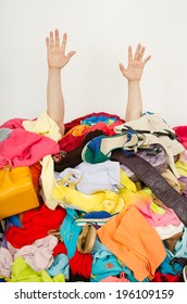 Man hands reaching out from a big pile of clothes and accessories. Man buried under an untidy cluttered woman wardrobe. Man reaching for help from to much woman shopping. - Shutterstock ID 196109159