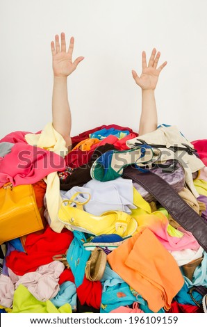 Man hands reaching out from a big pile of clothes and accessories. Man buried under an untidy cluttered woman wardrobe. Man reaching for help from to much woman shopping.