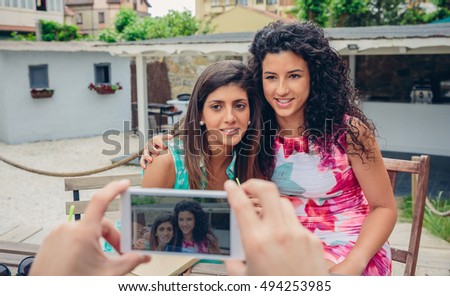 Männerhände fotografieren zwei glückliche Frauen im Freien.