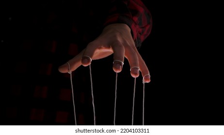 Man hands with threads or strings on fingers. The dictator's hand holds strings for manipulation on a black background. Close up human hand controls a puppet. Control concept.