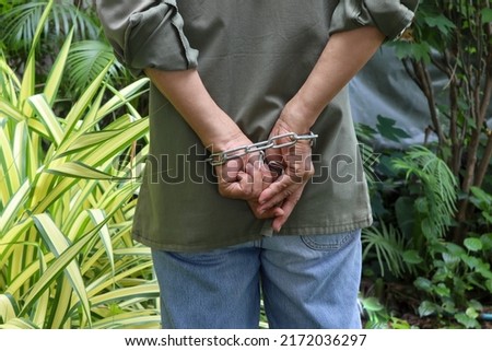 Man hands are tied to behind with steel chain in the garden closeup.