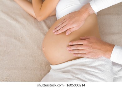 Man Hands Touching Pregnant Woman Belly. Lying Down On Bed. Body Health In Pregnancy Time. Relaxing Day. Closeup. Top View.