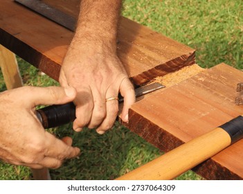 Man hands using a chisel to make cut in a wood plank. Closeup of man hands using a tool for carving a peroba wood plank.
