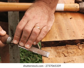 Man hands using a chisel to make cut in a wood plank. Closeup of man hands using a tool for carving a peroba wood plank.