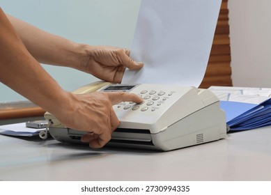 Man hands using a fax machine, putting paper in and sending fax in office