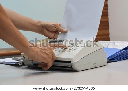 Man hands using a fax machine, putting paper in and sending fax in office