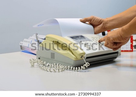 Man hands using a fax machine, putting paper in and sending fax in office