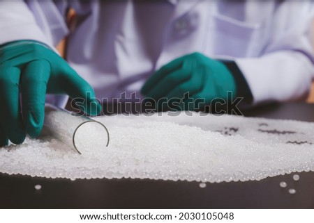 Man hands wearing gloves hold polymer pallet. Plastic beads on green gloved hand. polymer beads. The world's plastic reduction policy. plastic on black background.