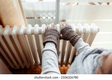 A Man Hands In Wool Gloves Warm Near The Heater. Old Men's Hands In Knitted Gloves On Heating Radiator At Home During The Day. Person Heating Their Hands At Home Over A Domestic Radiator In Winter.