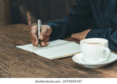 Man hands writing notebook diary with coffee cup and smartphone on wood desk. Close up man hands using pen sitting at wooden table outdoors lifestyle. Men write planner note diary office agenda - Powered by Shutterstock