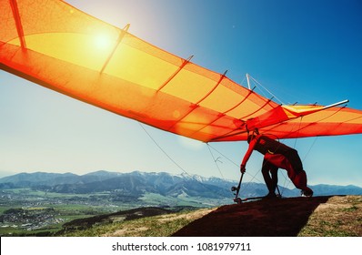 Man with hang-glider starting to fly from the hill top