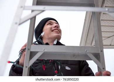 Man Hanging Christmas Lights During Winter From A Ladder