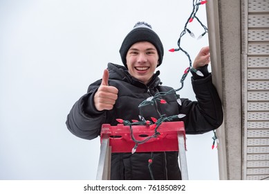 Man Hanging Christmas Lights During Winter From A Ladder