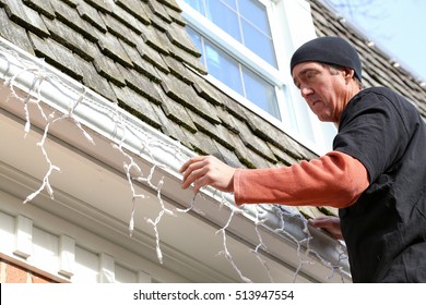 A Man Hanging Christmas Lights On The Exterior Of A House