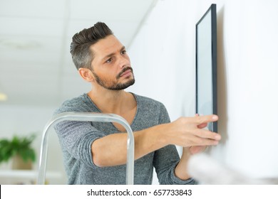 Man Hanging Picture Frames On Wall At Home