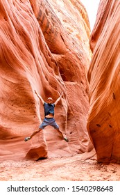 Man Happy Hiker Jumping Up Vertical View By Red Wave Shape Formations At Antelope Slot Canyon In Arizona On Footpath Trail From Lake Powell