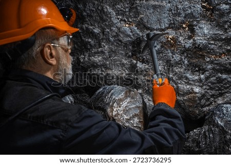 A man in a hard hat with a flashlight examines rock using a pickaxe. Geology, speleology, mining with a scientific approach