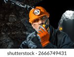 Man in a hard hat with a flashlight using a walkie-talkie in the darkness underground. Geology, speleology, cave rescue, mining with a scientific approach