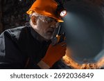 Man in a hard hat with a flashlight using a walkie-talkie in the darkness underground. Geology, speleology, cave rescue, mining with a scientific approach
