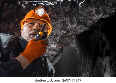 Man in a hard hat with a flashlight using a walkie-talkie in the darkness underground. Geology, speleology, cave rescue, mining with a scientific approach