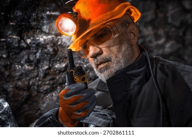 Man in a hard hat with a flashlight using a walkie-talkie in the darkness underground. Geology, speleology, cave rescue, mining with a scientific approach