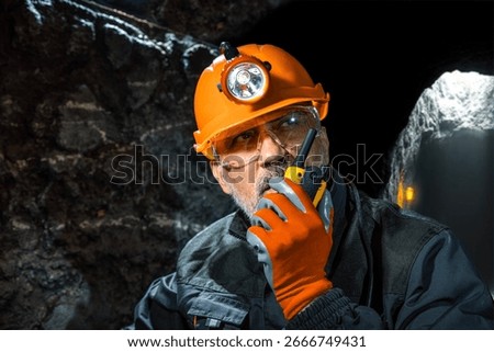 Man in a hard hat with a flashlight using a walkie-talkie in the darkness underground. Geology, speleology, cave rescue, mining with a scientific approach