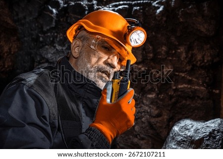 Man in a hard hat with a flashlight using a walkie-talkie in the darkness underground. Geology, speleology, cave rescue, mining with a scientific approach