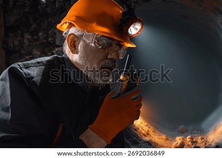 Man in a hard hat with a flashlight using a walkie-talkie in the darkness underground. Geology, speleology, cave rescue, mining with a scientific approach