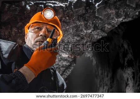 Man in a hard hat with a flashlight using a walkie-talkie in the darkness underground. Geology, speleology, cave rescue, mining with a scientific approach