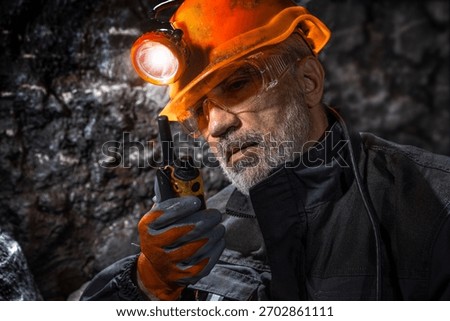 Man in a hard hat with a flashlight using a walkie-talkie in the darkness underground. Geology, speleology, cave rescue, mining with a scientific approach