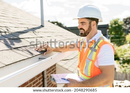 A man in a hard hat, holding a clipboard, standing on the steps of an old rundown house.