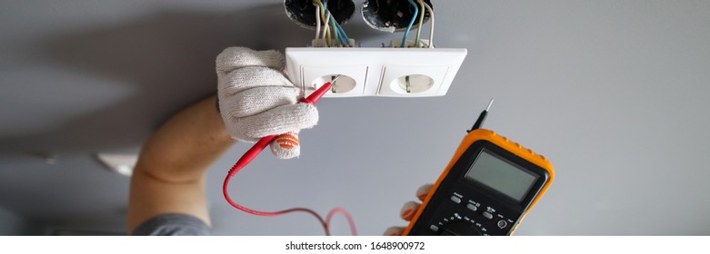 Man In Hard Hat And Protective Gloves Checking Wal Outlet With Tester Closeup