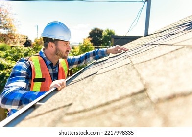 A man with hard hat standing on steps inspecting house roof - Shutterstock ID 2217998335