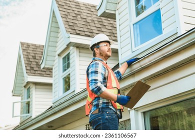 A man with hard hat standing on steps inspecting house roof - Shutterstock ID 2361106567