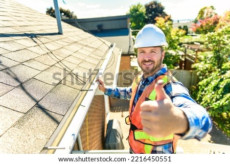 A man with hard hat standing on steps inspecting house roof