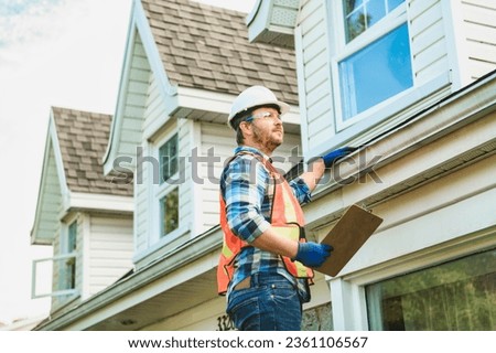 A man with hard hat standing on steps inspecting house roof