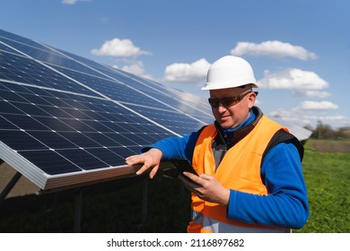 Man in hard hat using smartphone on the background of solar panels