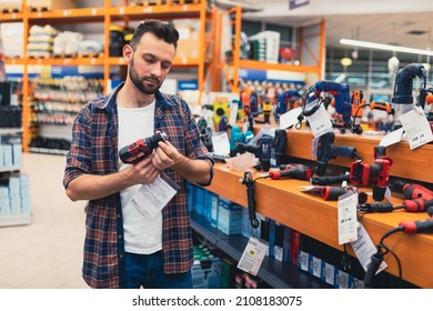 a man in a hardware store chooses a new screwdriver next to a showcase of power tools for repairs in the house