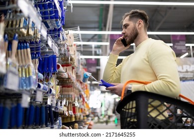 A Man In A Hardware Store Chooses Paint Brushes While Discussing It On The Phone With His Wife