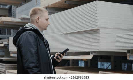 A man in a hardware store chooses wooden sheets of osb. The buyer in the store chooses chipboard. Buying plywood at a hardware store. Blockboards in a hardware store - Shutterstock ID 2362996583