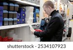 A man in a hardware store choosing a toolbox. Customer comparing plastic storage boxes in hardware store aisle, choosing best option for tools and equipment organization. Essential for home projects