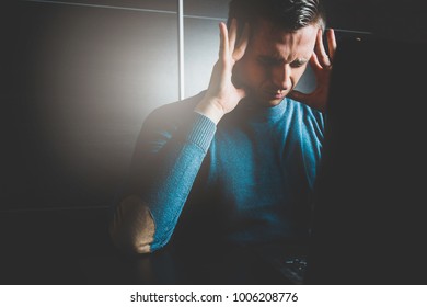 A man has a headache while working on a laptop. Hard work and headache. Medical and pharmaceutical concept. The man is holding his hand by the head, he has a dissatisfied face.