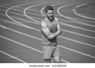 Man Has Injury After Exercise On Stadium. Fitness Gym Outdoor. Muscular Athletic Guy With Bruise. Sport Training. Male Trauma. Sportsman Athlete Flex Muscles And Knead A Joint. Feel Pain