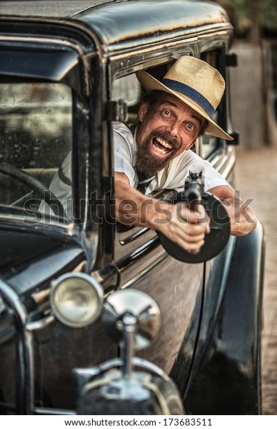 Man in hat and\
beard shooting gun from old\
car