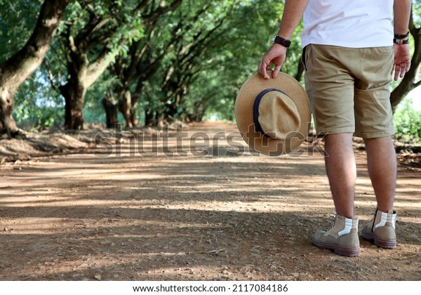 man with hat and boots in the middle of dirt road
and trees