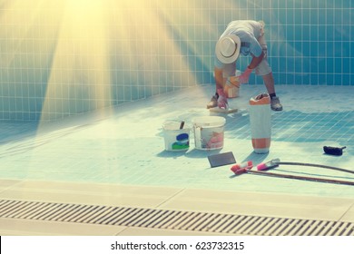 Man in a hat put the tiles on the bottom of the poolin the sunlight . Toned
