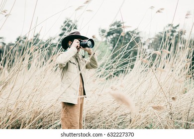 Man with hat standing between reed photographing nature.